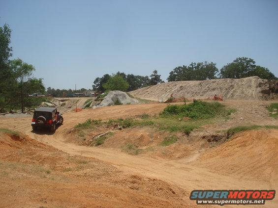 Red Jeep Wrangler driving on a dirt track at an off-road park