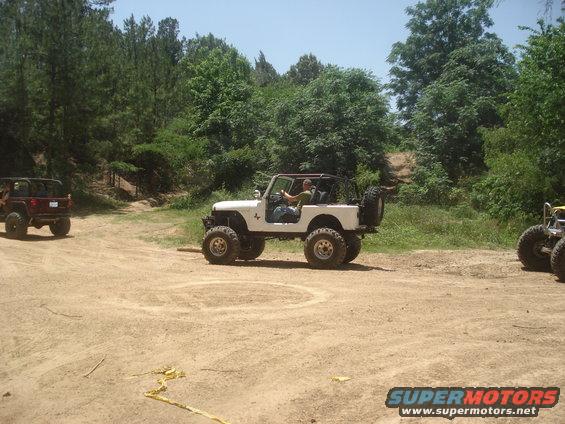 White off-road jeep with a spare tire on the back drives on a dirt path