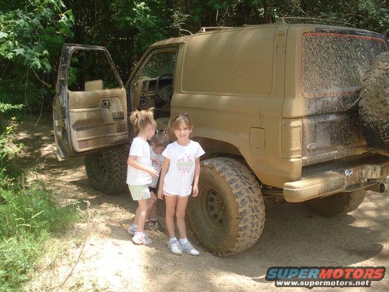 Muddy 1989 Ford Bronco II with door open and three girls standing next to it