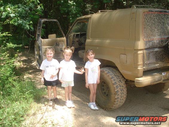 Tan 1989 Ford Bronco II with open driver door and large tires parked on a dirt road