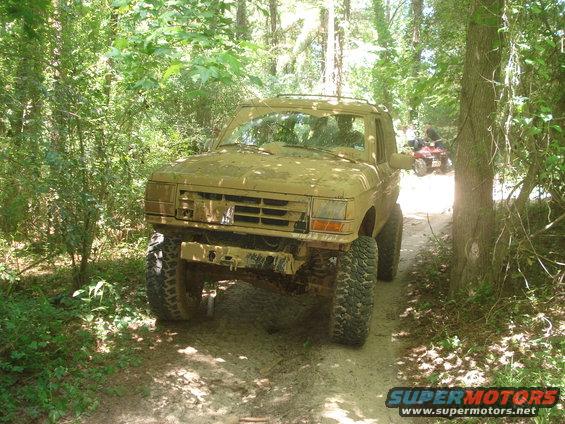 Mud-covered 1989 Ford Bronco II on a wooded trail with an ATV in the background