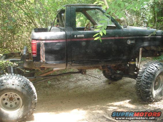 Modified black SUV with large tires and snorkel, parked in woods