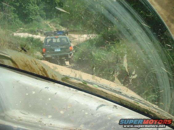 Mud-splattered 1989 Ford Bronco II driving on a dirt road, seen from inside another vehicle