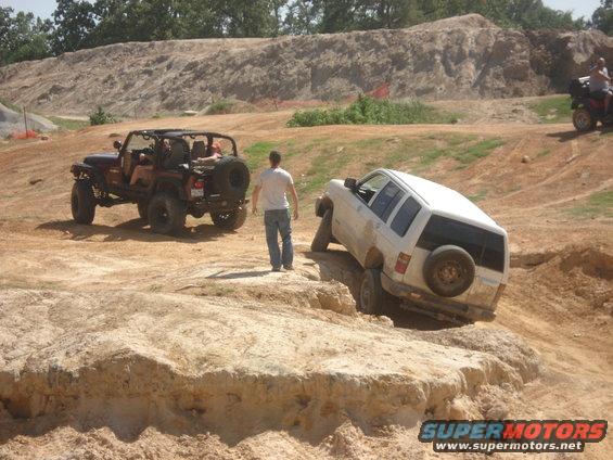 Jeep and white SUV off-roading on dirt hills. Guy watches
