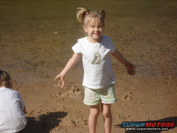 Two young girls with ponytails on a sandy beach, one in a white t-shirt with a cat graphic and patterned shorts