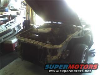 Car front end disassembled in garage, another car partially visible to the left
