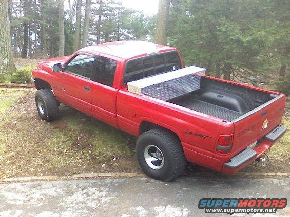 1997 Dodge 1500 pickup truck, red, with a silver toolbox in the bed, parked on a grassy area next to a paved surface