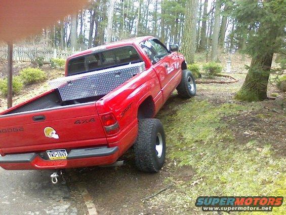 Red Dodge pickup truck with a toolbox in the bed, parked on a grassy incline