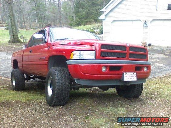 Red 1997 Dodge 1500 pickup truck with lifted suspension and large tires, parked on grass in front of a garage