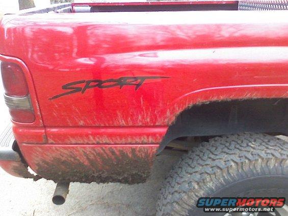 Red pickup truck rear quarter panel with "SPORT" decal and mud splatter