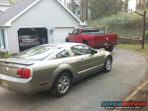Silver Ford Mustang coupe parked on driveway with red pickup truck behind it