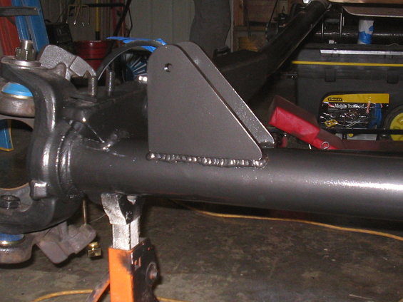 Close-up of a dark gray vehicle axle with a welded bracket, supported by an orange jack stand