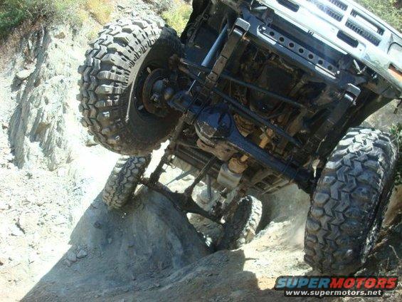 Off-road truck climbing a steep, rocky incline, showing its undercarriage and large tires
