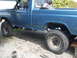 1984 Ford F-150 - Side view of a lifted blue pickup truck with large off-road tires and a spare tire in the bed.