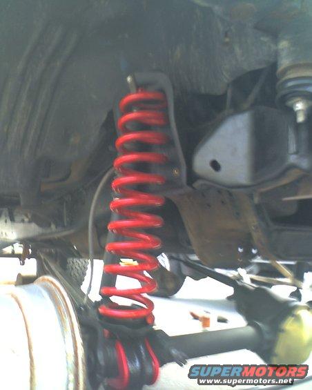 Close-up of a red coil spring and suspension parts under a vehicle