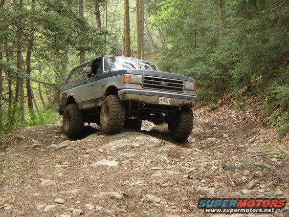 Ford Bronco on rocky trail, dark blue and grey two-tone paint, lifted suspension, off-road tires