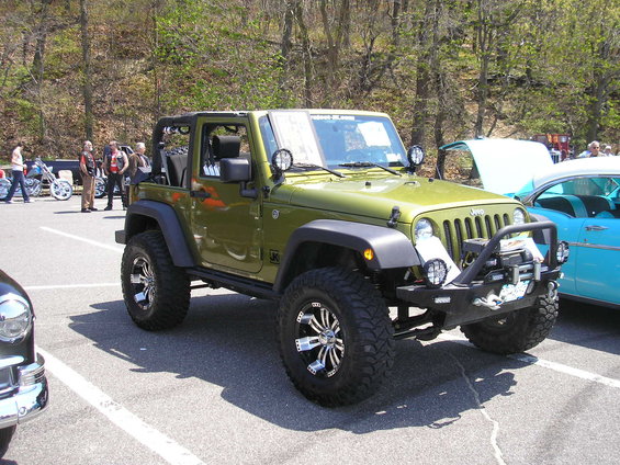 Green Jeep Wrangler with aftermarket bumper and large tires parked on asphalt