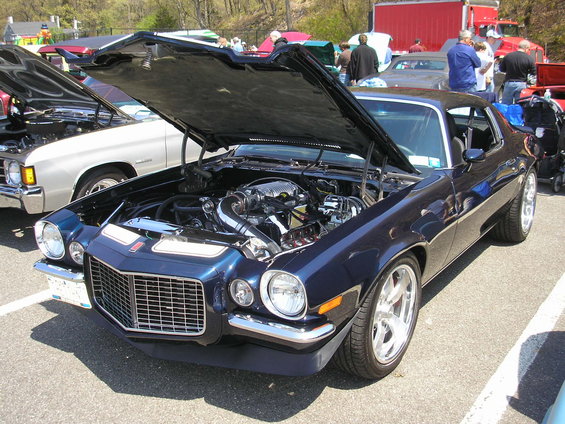 Dark blue coupe, hood open, showing engine. Custom wheels. Other cars visible