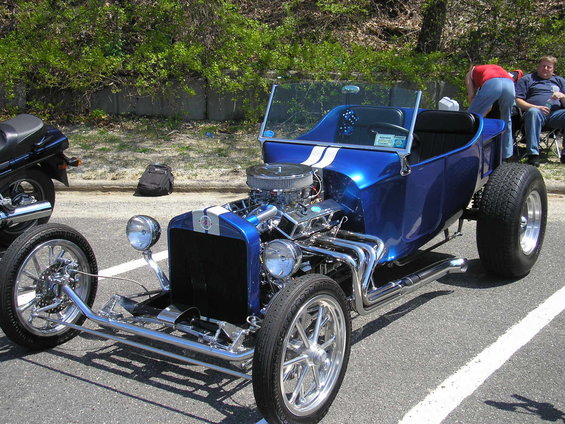 Blue hot rod with exposed engine and white racing stripes, parked on asphalt