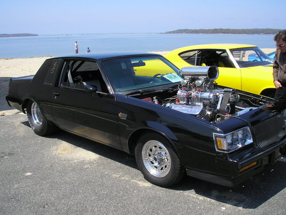 Black Buick Regal modified with a supercharger, parked next to a yellow car by the beach