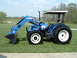 1984 Honda ATC 250 R - A blue New Holland tractor with a front loader is shown from a three-quarter front angle on a grassy area.