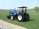1984 Honda ATC 250 R - A blue tractor with a front loader sits on a green lawn under a clear sky.