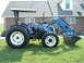 1984 Honda ATC 250 R - A blue New Holland tractor equipped with a front loader is shown from the side on a grassy lawn.
