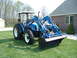 1984 Honda ATC 250 R - A blue tractor with a front loader is parked on a lawn near a house.