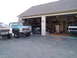 1979 Ford Bronco - Three pickup trucks are parked outside a garage. The green truck in the foreground is a 1979 Ford Bronco.