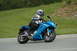 2007 Kawasaki Ninja R - A rider on a blue Kawasaki Ninja motorcycle is seen from the front-three-quarter angle on a paved road with a grassy hill in the background.