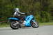 2007 Kawasaki Ninja R - A rider on a blue 2007 Kawasaki Ninja R motorcycle cruises down a road with trees in the background.