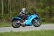 2007 Kawasaki Ninja R - A rider on a blue 2007 Kawasaki Ninja R motorcycle rides down a road with trees in the background.