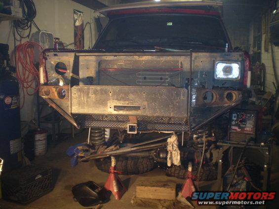 Front end of a vehicle with grille removed, being worked on in a garage