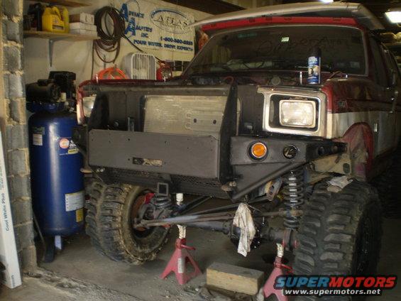 Red and silver Ford Bronco front end with custom bumper, off-road tires, and jack stands