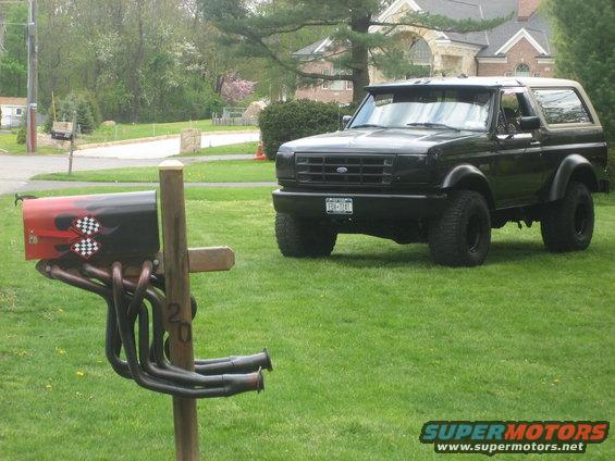 Black Ford Bronco parked on grass next to a custom mailbox with exhaust pipes