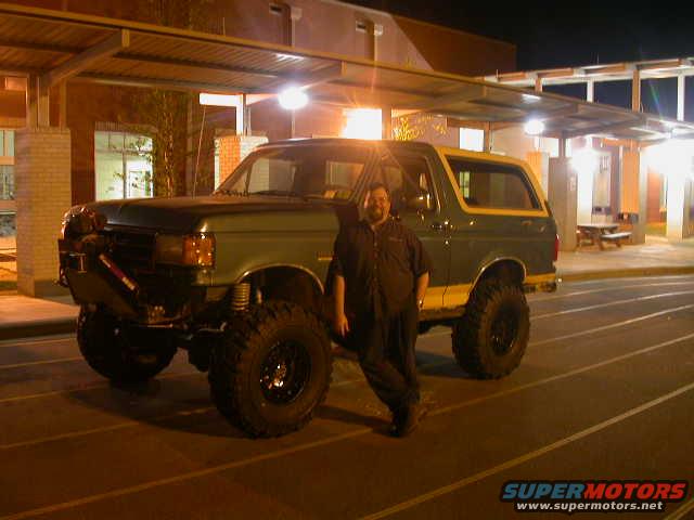Man standing next to a lifted green and yellow Ford Bronco with large tires