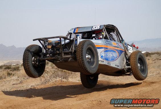 Off-road buggy with number 2025 airborne over a dirt track
