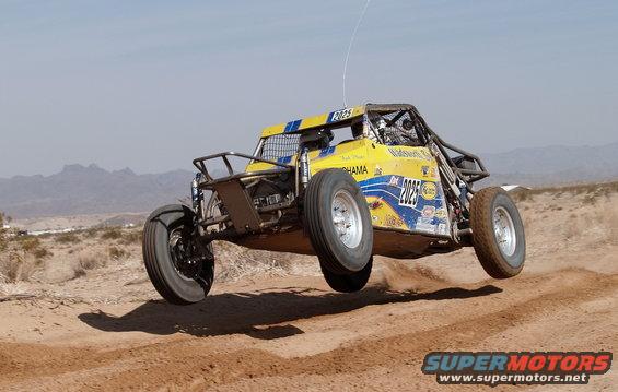 Yellow off-road buggy mid-air over a dirt track