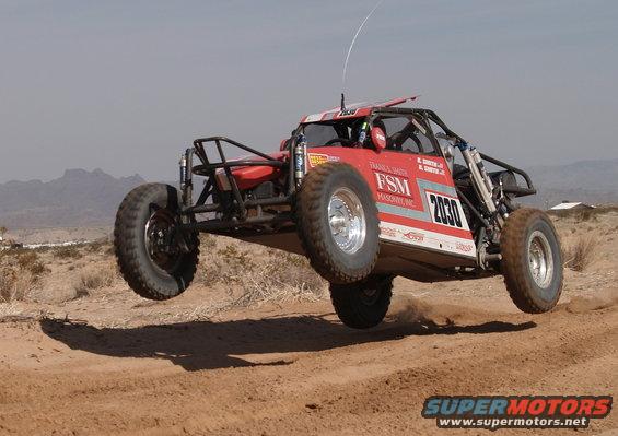 Red off-road buggy with number 2030 airborne over a dirt track
