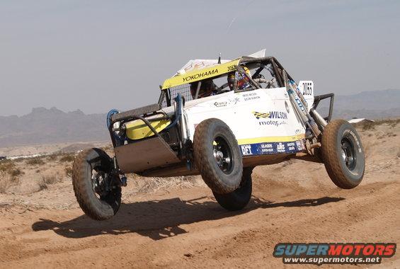 Off-road buggy with Yokohama tires airborne over a dirt track. Number 2055 is visible on the side