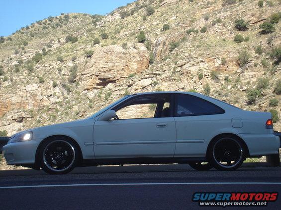 White coupe parked on roadside with mountains in background