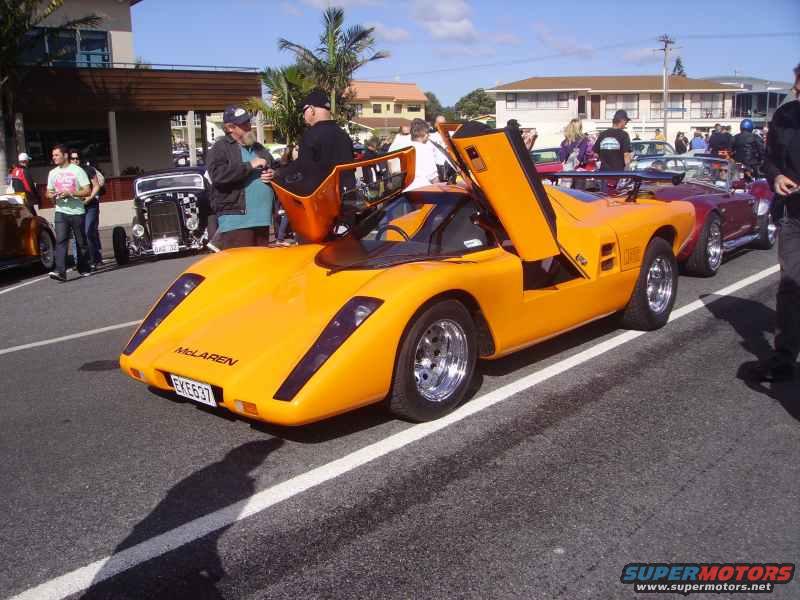 Orange McLaren sports car with gullwing doors open, license plate EKE637