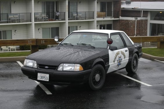 Black and white police car with "HIGHWAY PATROL" text on door, parked in a lot