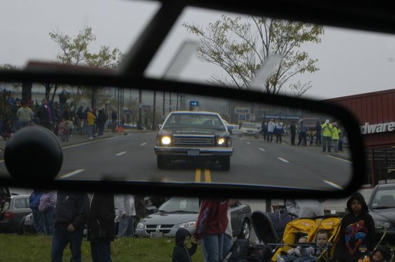 police car with lights on driving down street, seen in rearview mirror