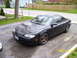 1997 Mazda MX-6 - A black coupe with aftermarket bronze wheels is parked on a gravel driveway.