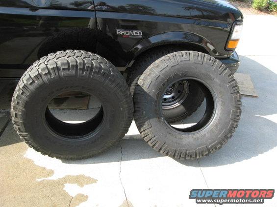 Two large off-road tires in front of a black 1996 Ford Bronco