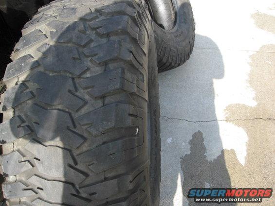 Close-up of a large, knobby off-road tire with a shadow cast on the concrete ground
