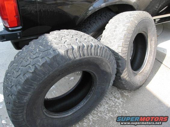 Three off-road tires, one mounted on a black vehicle's rear wheel well