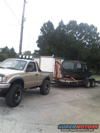Tan Toyota Tacoma towing a trailer with a black vehicle body on it
