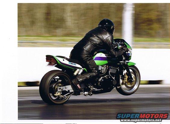 Green and purple motorcycle with a rider in black leather, performing a wheelie on a track